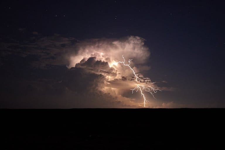 A powerful lightning storm illuminates the night sky with dramatic flashes over a vast landscape, representing the storms we endure and survive in life.